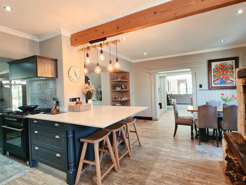 Spacious open-plan kitchen and dining area featuring a large island, modern gas stove, exposed timber beam, and a cozy stone fireplace.