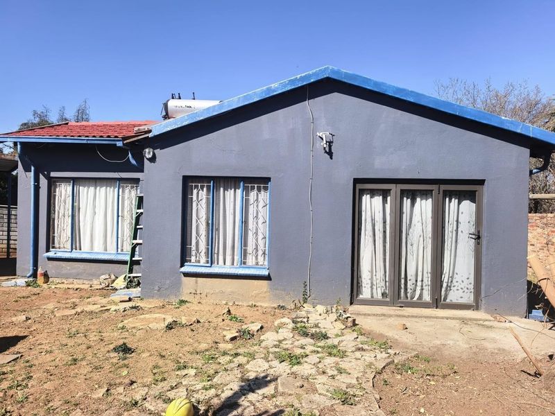 Rear view of the house featuring a solar water heater, security bars on windows, and a sliding glass door leading to a concrete patio area.