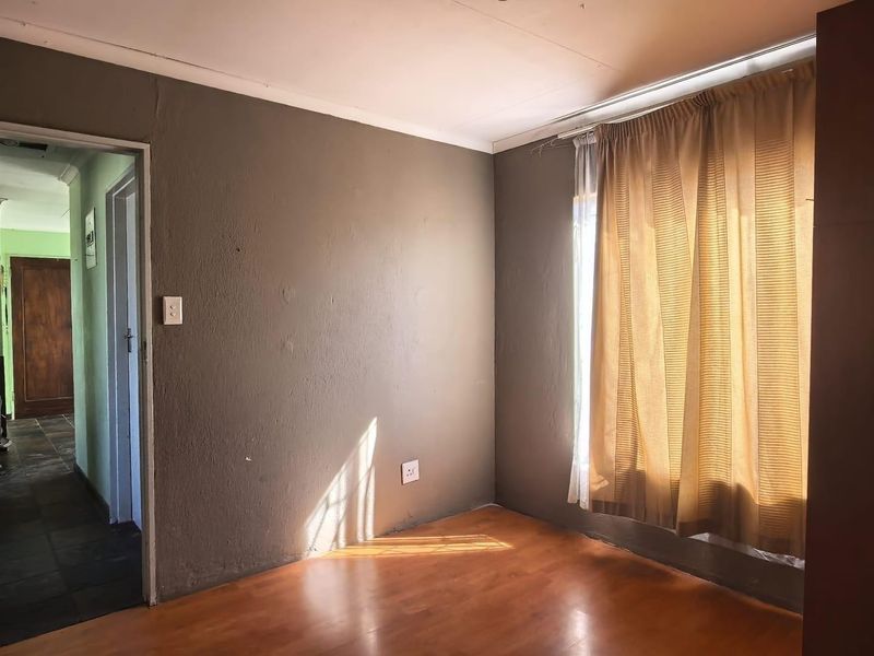 An empty bedroom featuring laminate flooring and a window with curtains, providing a blank canvas for potential interior design updates.