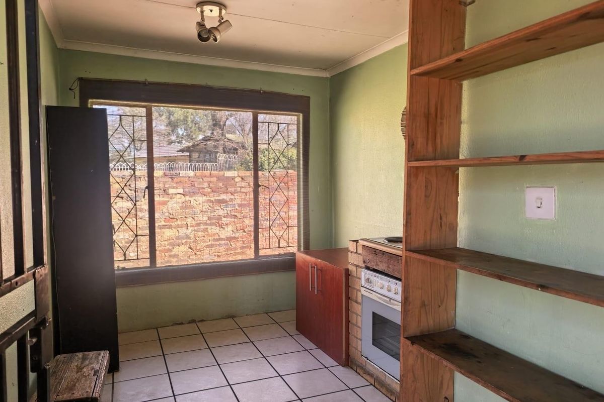 A compact kitchen featuring tiled floors, built-in oven and hob, and open shelving, offering a functional space ready for modernization and cosmetic updates.