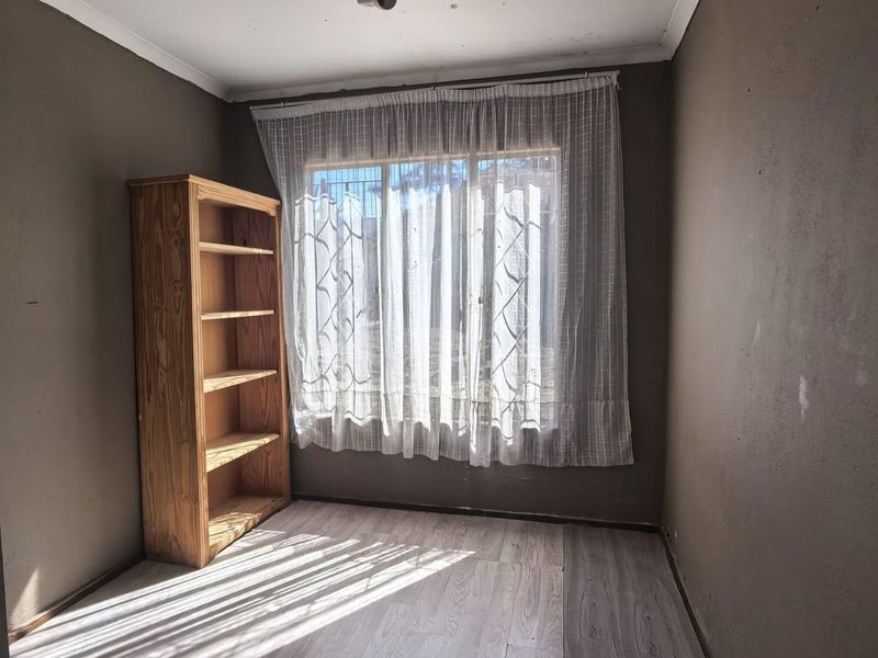 A vacant bedroom featuring laminate flooring, window security bars, and neutral wall tones, offering a blank canvas for renovation or interior design updates.