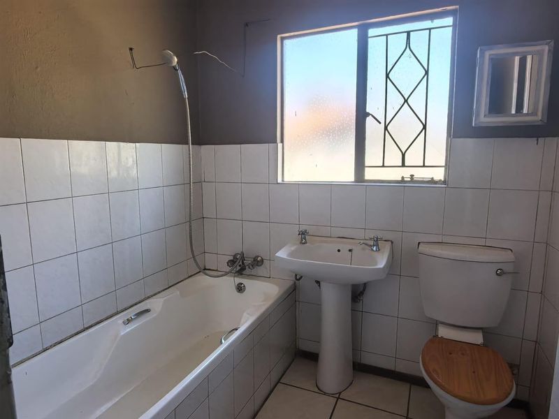 A functional bathroom featuring a bathtub, pedestal basin, and toilet, with tiled finishes and security bars on the window.