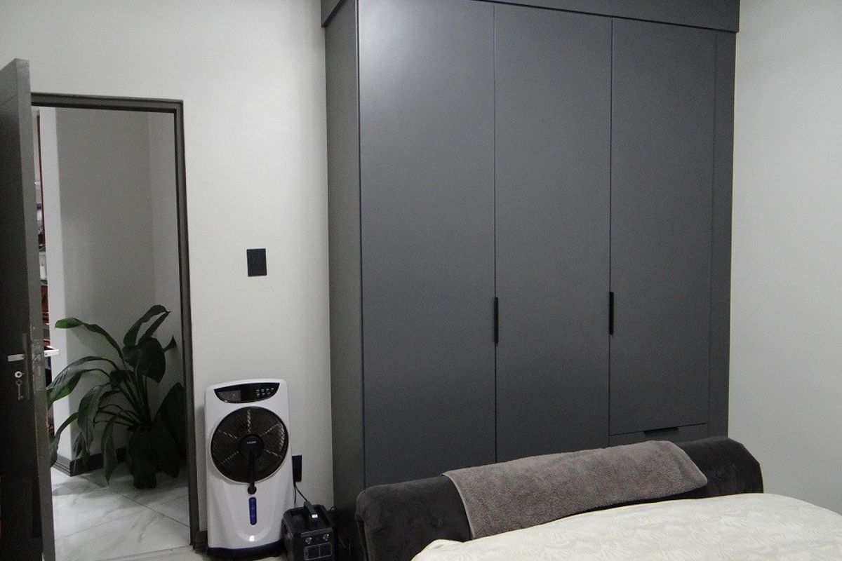 A bedroom featuring a modern, dark grey built-in wardrobe with clean lines and minimalist hardware.