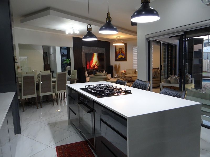 Modern open-plan living area featuring a sleek kitchen island with integrated gas hob and oven, flowing seamlessly into the dining and lounge space.