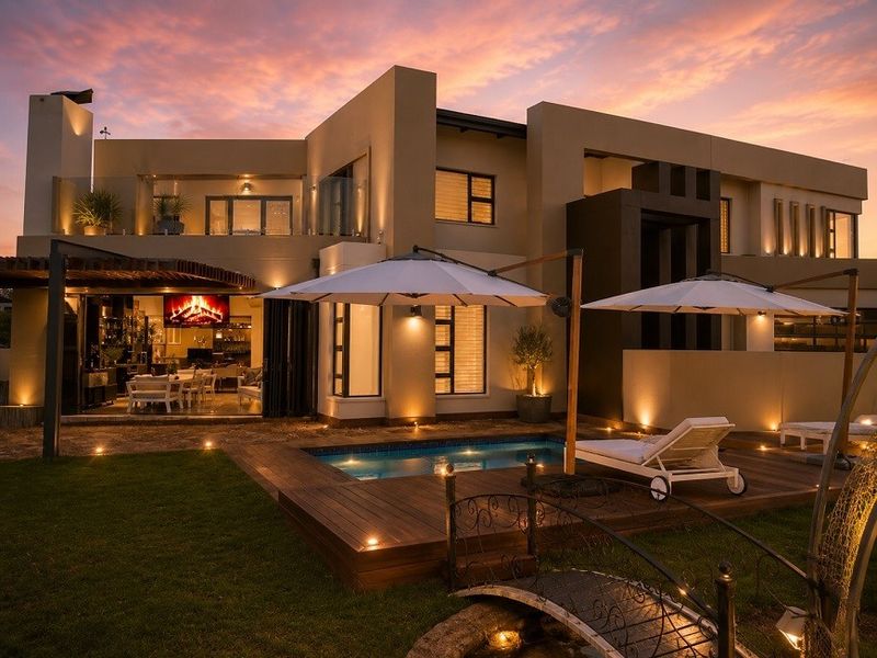 Stunning rear elevation featuring a modern swimming pool, timber decking, covered patio with fireplace, and sophisticated exterior lighting at dusk.