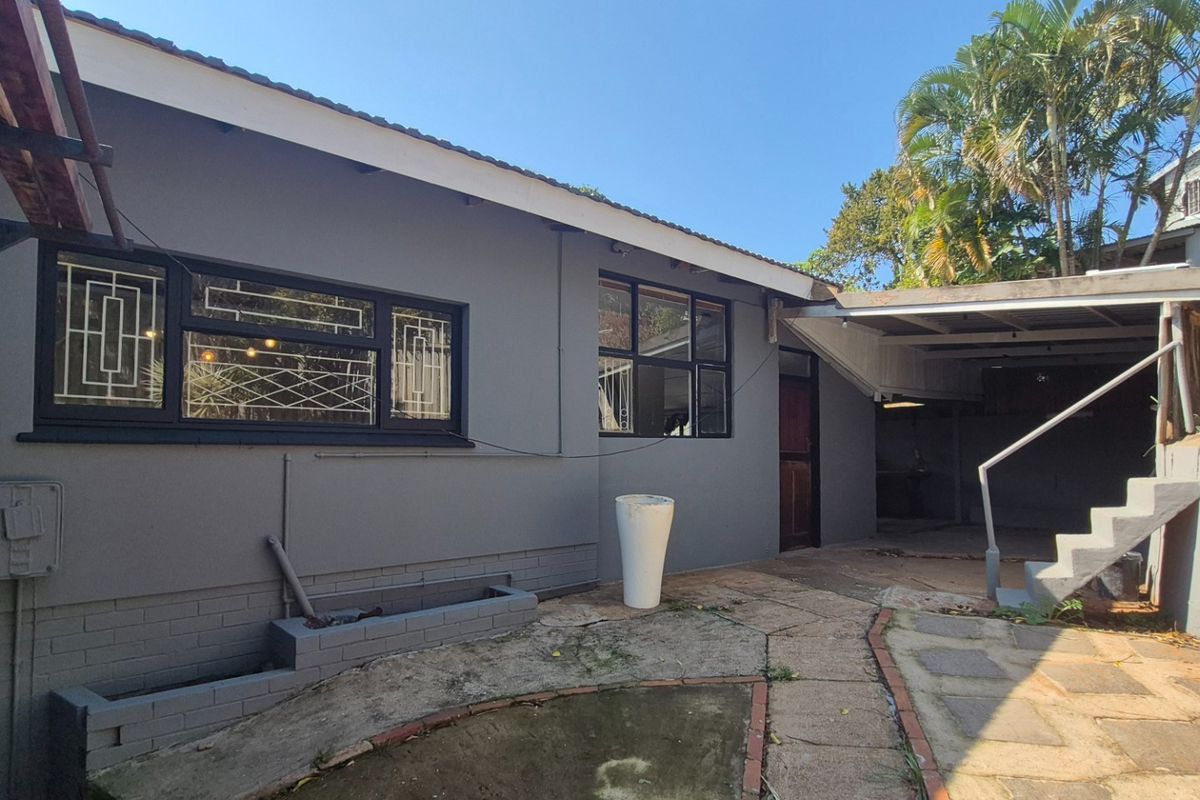 Rear exterior view of the property featuring a paved walkway, concrete stairs, and a covered patio area with security-barred windows.