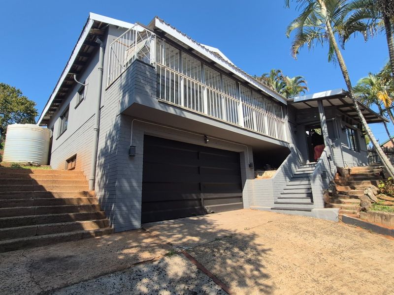 Front exterior view of a multi-level house featuring a garage, elevated balcony with security bars, and concrete staircase access.