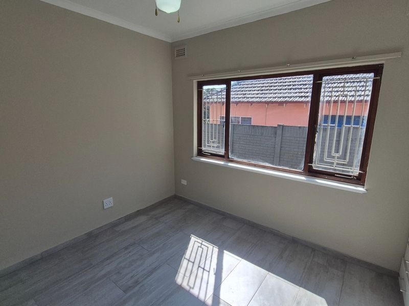 A clean, empty bedroom featuring neutral walls, modern tiled flooring, and built-in cupboards with security bars on the window.