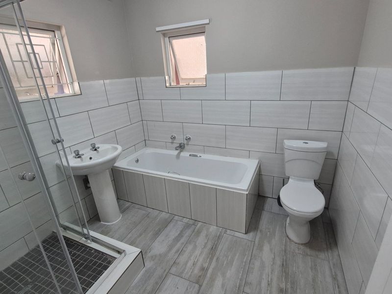 A clean, modern bathroom featuring a pedestal basin, built-in bathtub, glass shower enclosure, and toilet with neutral tiled finishes.
