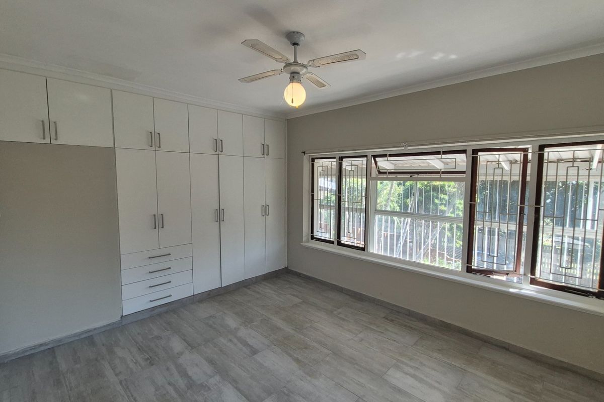 Spacious bedroom featuring extensive built-in cabinetry, modern tiled flooring, a ceiling fan, and large windows fitted with security bars.