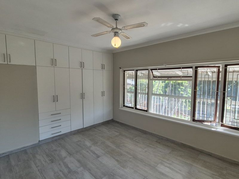 Spacious bedroom featuring extensive built-in cabinetry, modern tiled flooring, a ceiling fan, and large windows fitted with security bars.