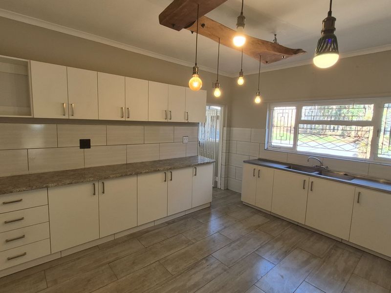 A clean, modern kitchen featuring white cabinetry, granite countertops, tiled backsplash, and unique pendant lighting, offering a bright and functional workspace.