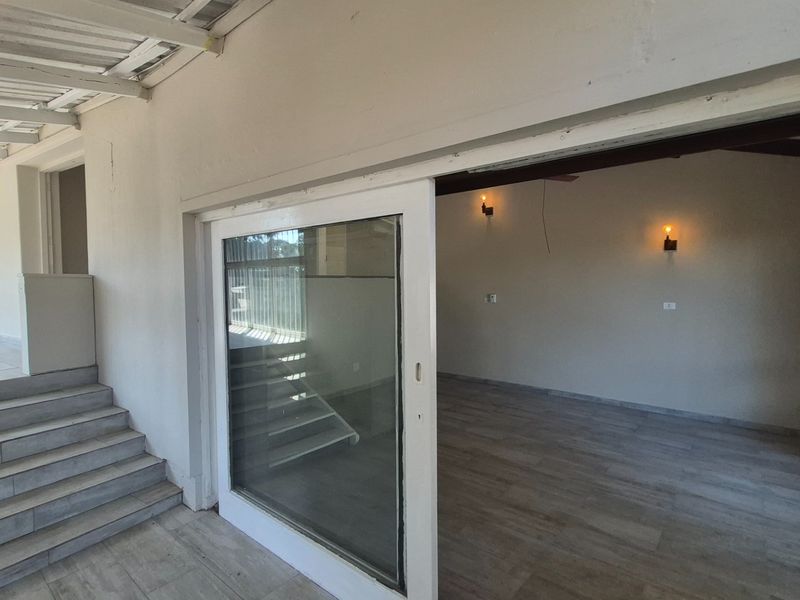 A covered patio area featuring tiled flooring, exposed beam ceilings, and a large sliding glass door leading into an interior living space.
