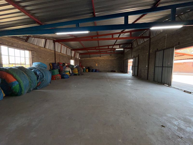 Spacious industrial utility area featuring exposed steel roof trusses, concrete flooring, and large sliding metal doors, suitable for storage or workshop use.