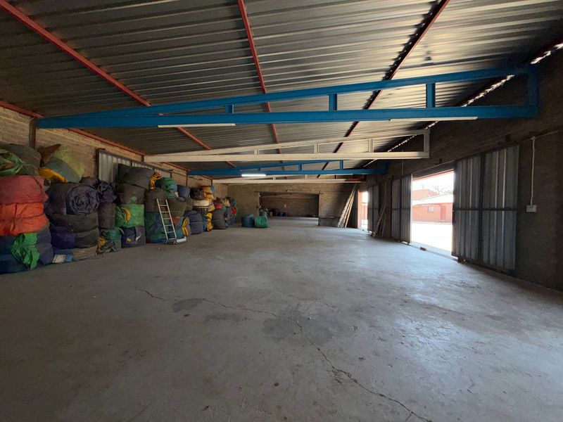 Spacious industrial warehouse unit featuring exposed steel roof trusses, concrete flooring, and large sliding metal doors for easy access.