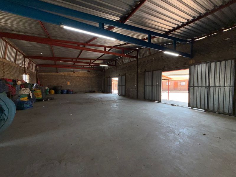 Spacious industrial utility area featuring exposed steel roof trusses, concrete flooring, and large sliding metal doors providing ample access.