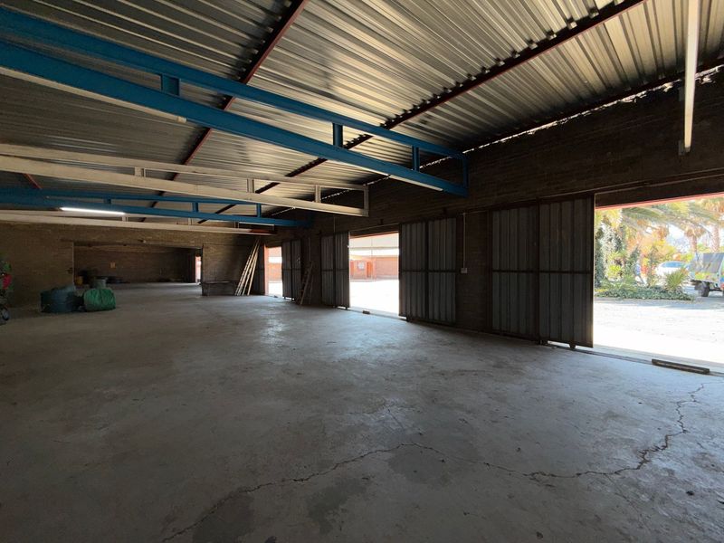 Spacious industrial utility area featuring exposed steel roof trusses, concrete flooring, and large sliding doors providing access to the exterior.
