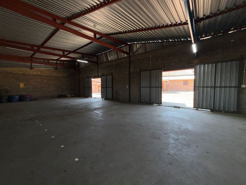Spacious industrial warehouse featuring exposed brick walls, concrete flooring, high-clearance steel roof trusses, and large sliding metal doors for easy access.