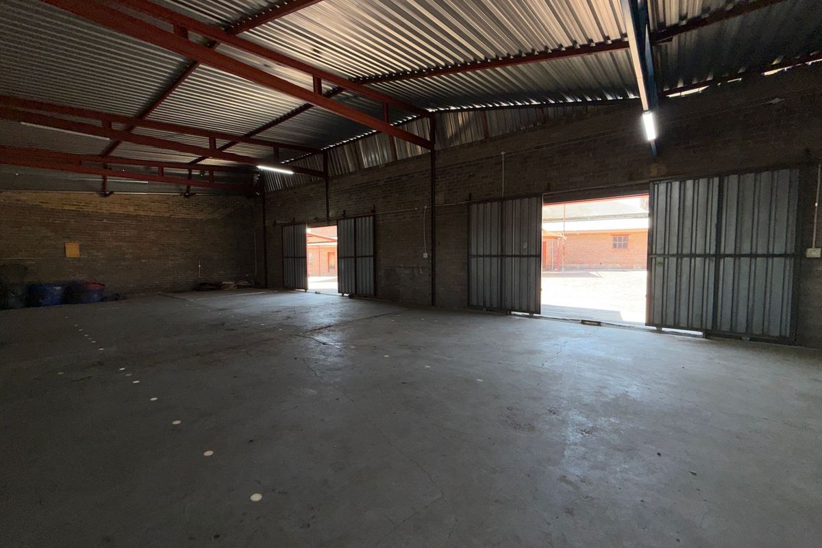 Spacious industrial warehouse featuring exposed brick walls, concrete flooring, high-clearance steel roof trusses, and large sliding metal doors for easy access.