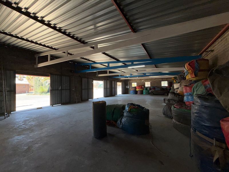 Spacious industrial utility area featuring exposed steel trusses, corrugated metal roofing, concrete flooring, and large sliding metal doors for easy access.