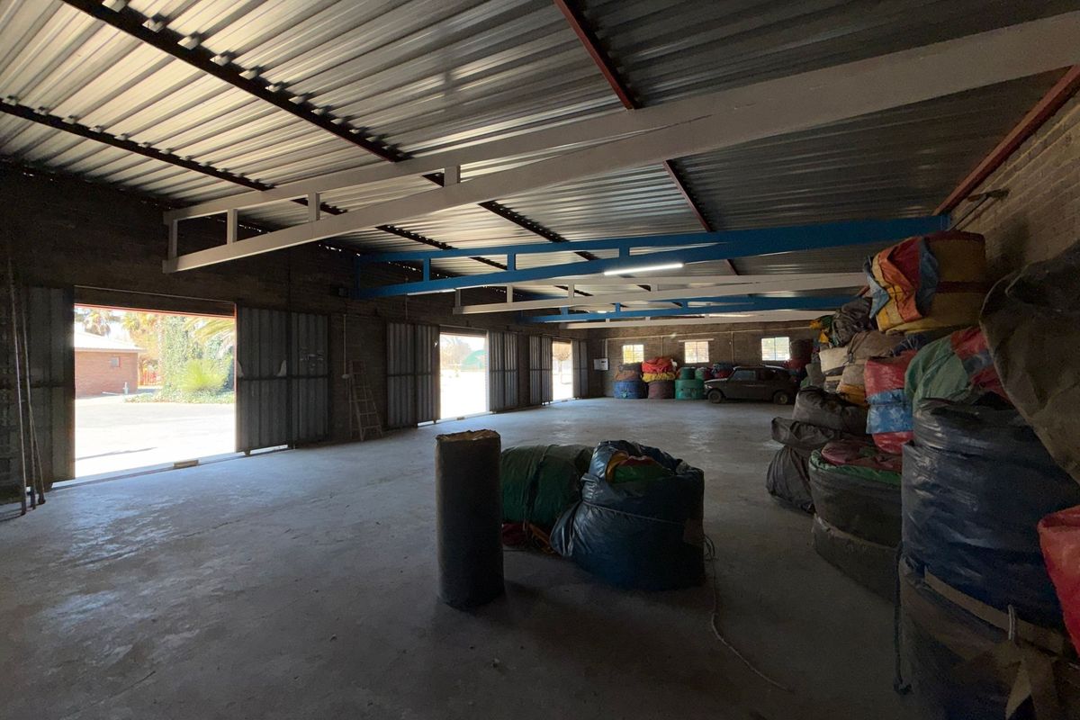 Spacious industrial utility area featuring exposed steel trusses, corrugated metal roofing, concrete flooring, and large sliding metal doors for easy access.