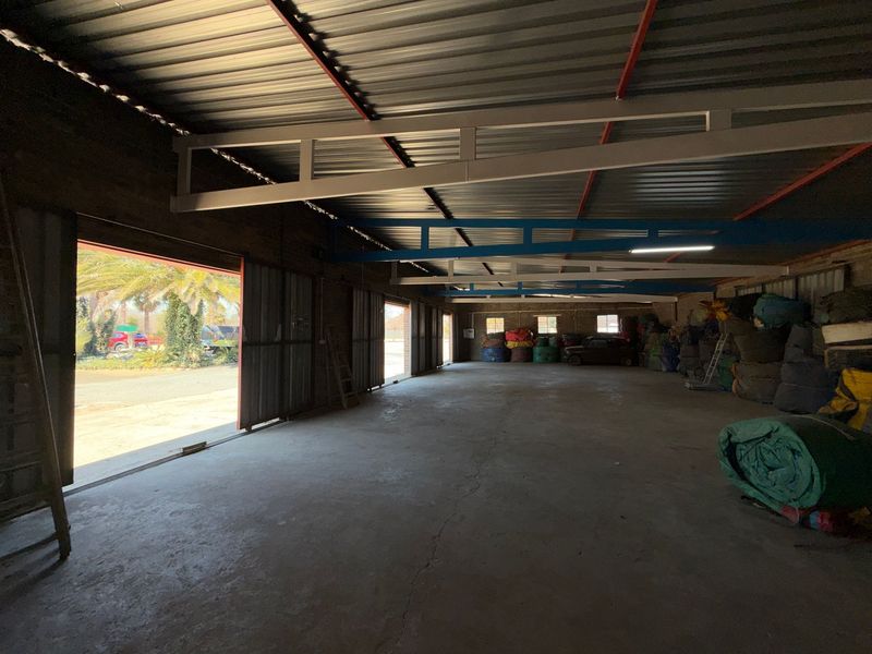 Spacious industrial utility area featuring exposed steel roof trusses, concrete flooring, and large sliding metal doors providing access to the exterior.