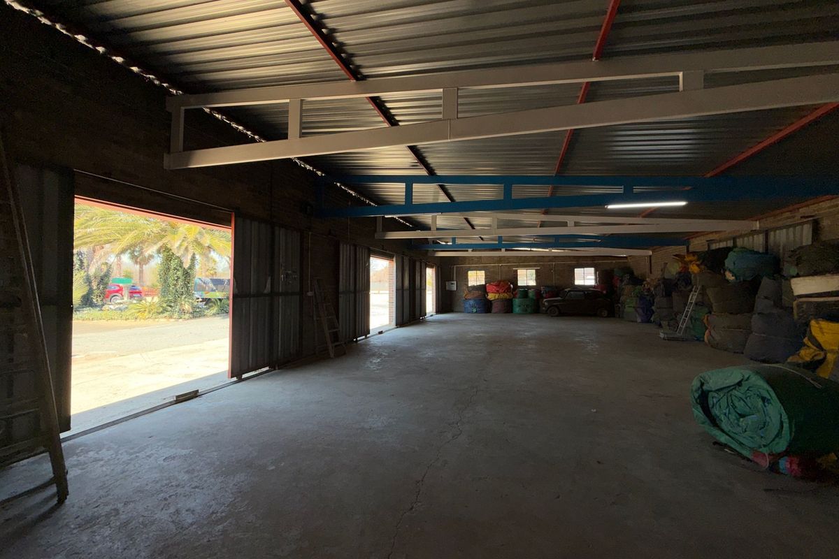 Spacious industrial utility area featuring exposed steel roof trusses, concrete flooring, and large sliding metal doors providing access to the exterior.
