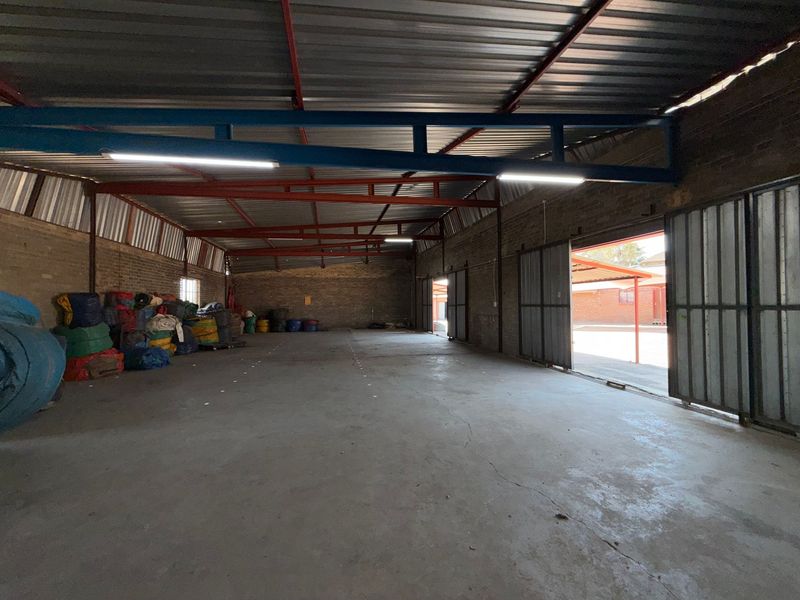 Spacious industrial warehouse unit featuring exposed steel roof trusses, concrete flooring, and large sliding metal doors providing easy access.
