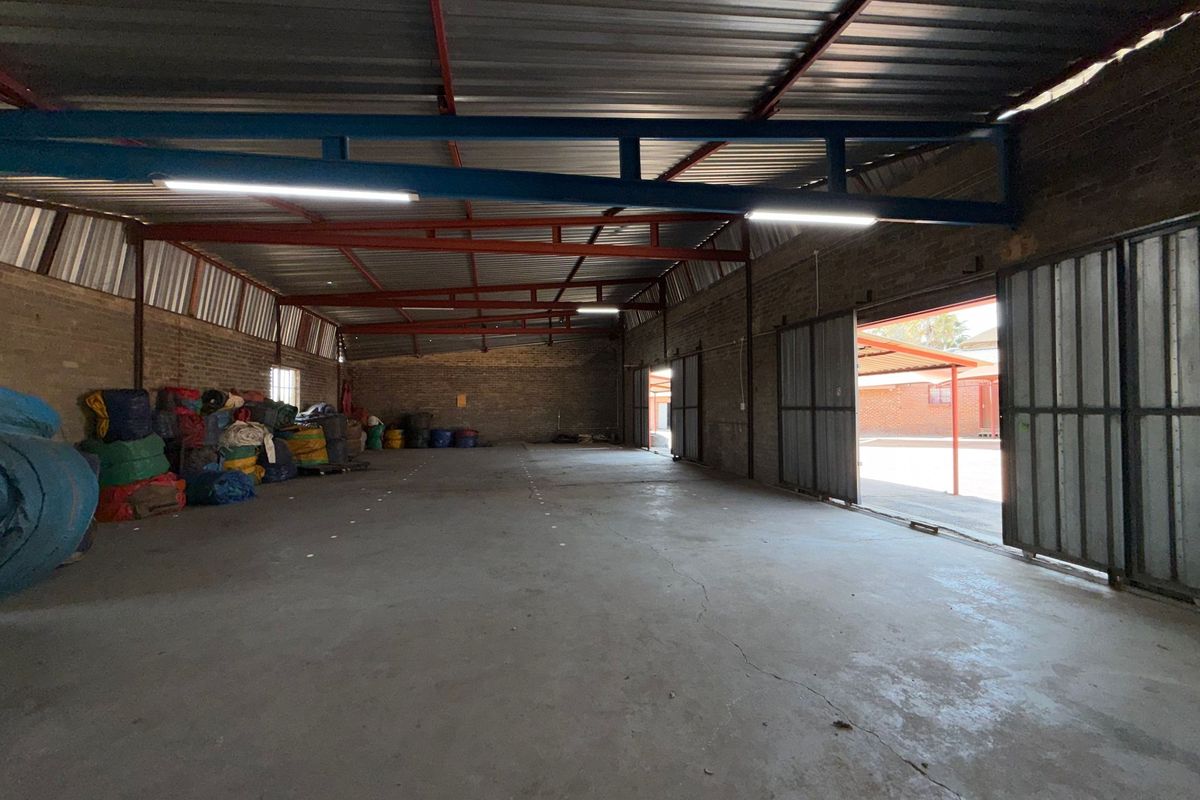 Spacious industrial warehouse unit featuring exposed steel roof trusses, concrete flooring, and large sliding metal doors providing easy access.
