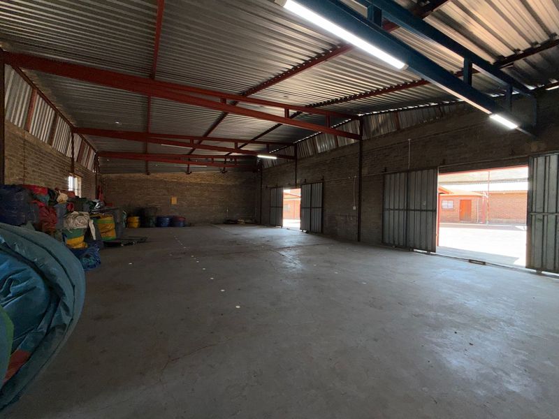 Spacious industrial utility area featuring exposed steel roof trusses, concrete flooring, and large sliding metal doors providing access to the exterior.