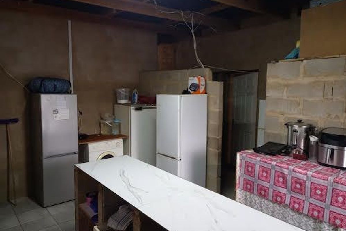 A rustic kitchen area featuring exposed concrete block walls, timber ceiling beams, and a central island, currently requiring significant finishing and renovation.