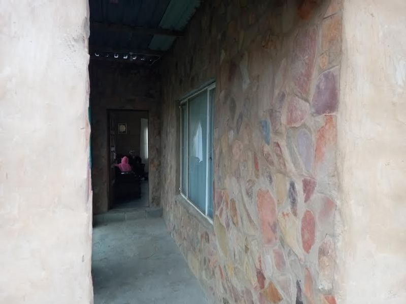 A covered outdoor walkway featuring rustic stone cladding, concrete flooring, and a sliding window, providing access to the interior living space.