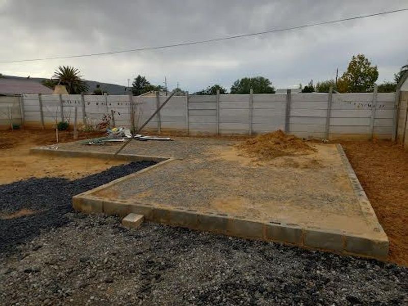 An outdoor area under construction featuring a concrete foundation slab and a precast concrete boundary wall.