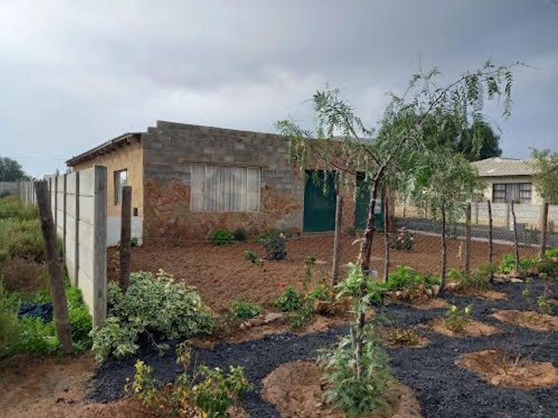Rear view of a house featuring exposed brick and stone cladding, with a large garden area enclosed by a concrete boundary wall.