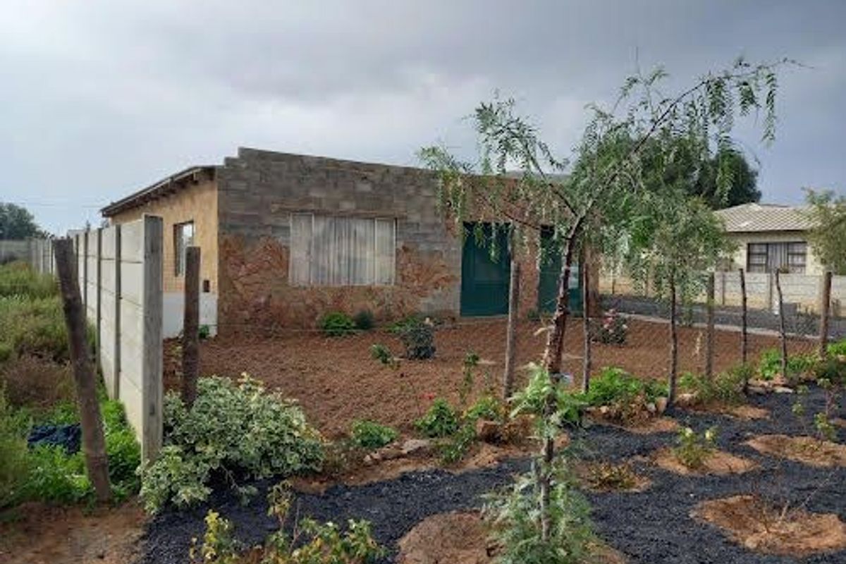 Rear view of a house featuring exposed brick and stone cladding, with a large garden area enclosed by a concrete boundary wall.