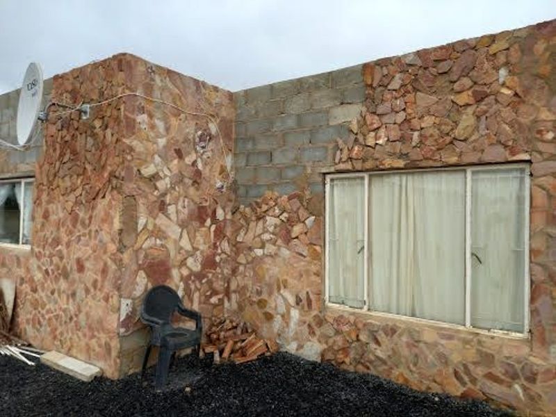 Exterior view of the property featuring partial stone cladding, exposed concrete blockwork, and aluminium-framed windows with security bars.