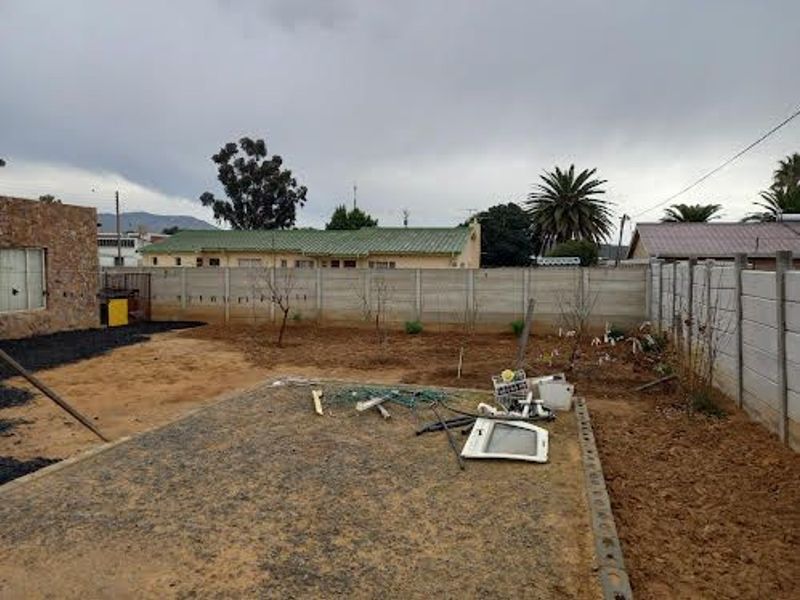 A rear yard area featuring a precast concrete boundary wall, gravel base, and unlandscaped soil, offering potential for garden development.