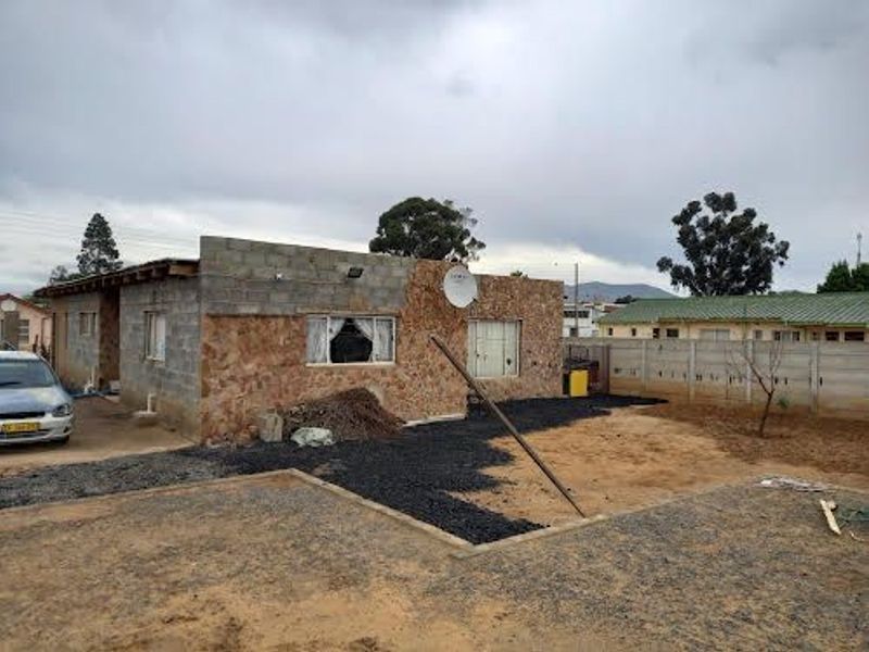 Front view of a house featuring stone cladding, concrete block construction, and a precast boundary wall on a large, undeveloped plot.
