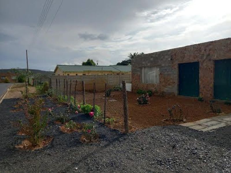 Front exterior view of a stone-clad house featuring a wire mesh fence, paved walkway, and a landscaped garden area.