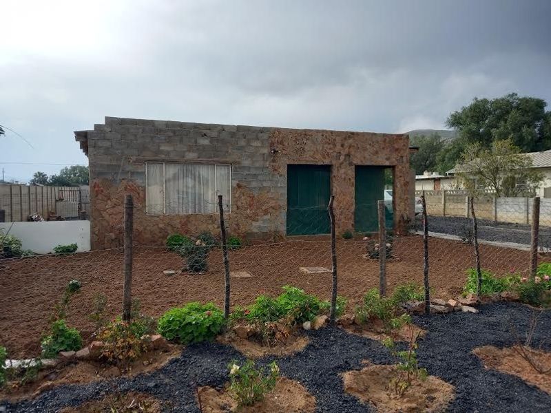 Front view of a house featuring a combination of stone cladding and unfinished concrete block masonry with a fenced garden area.