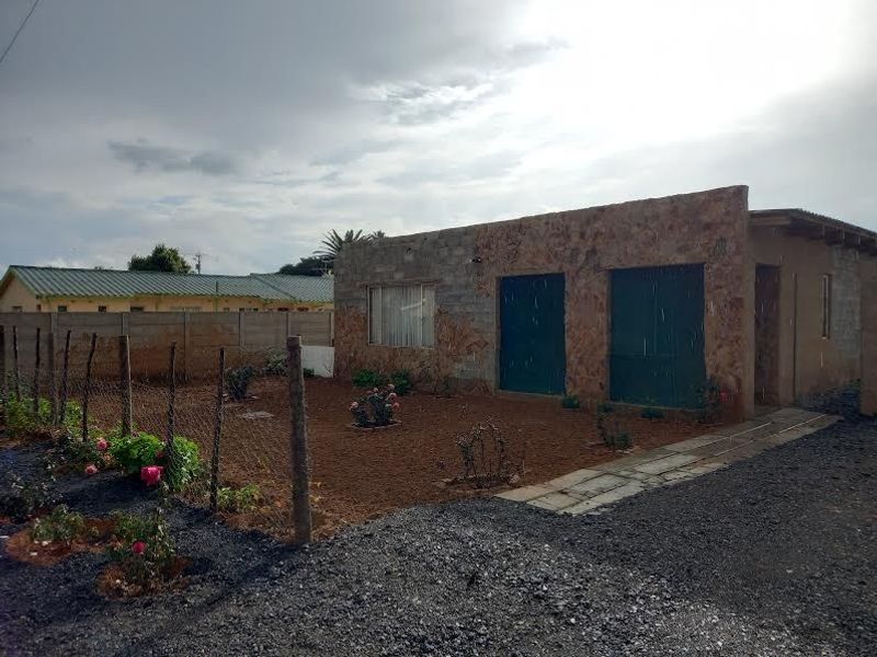 Rear view of a house featuring stone and concrete block construction, a fenced yard area, and a concrete pathway.