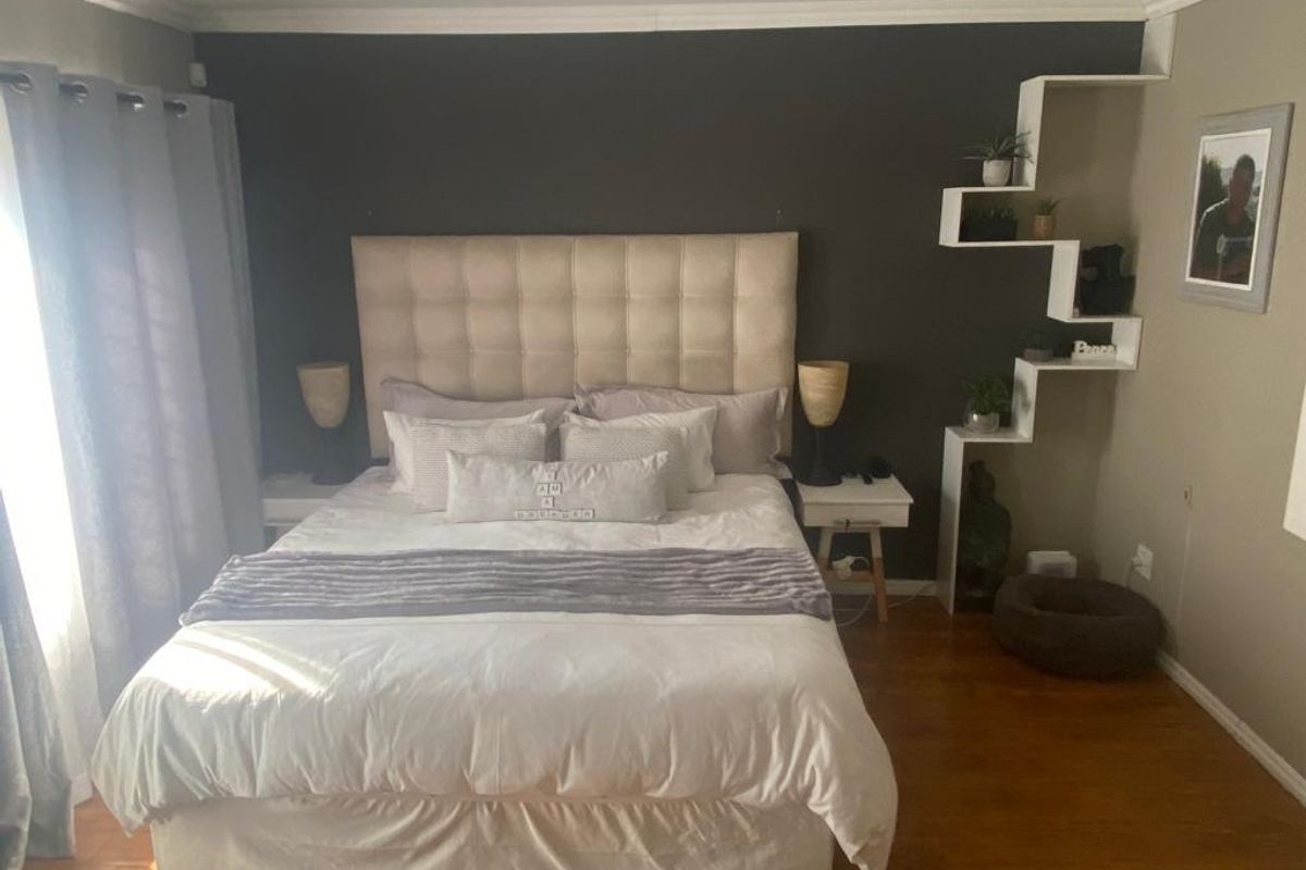 A well-maintained bedroom featuring hardwood flooring, crown molding, and a unique built-in stepped shelving unit against a dark accent wall.