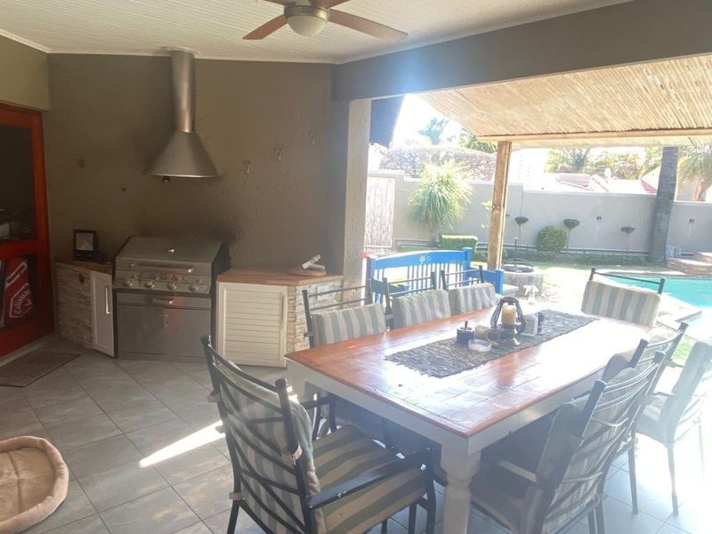 Covered outdoor patio featuring a built-in braai with stainless steel extractor hood, tiled flooring, and direct access to the garden and pool area.