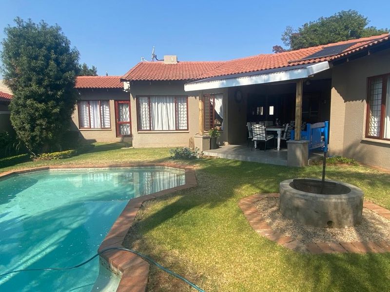Rear view of the property featuring a swimming pool, a covered patio area, and a built-in fire pit set within a landscaped garden.