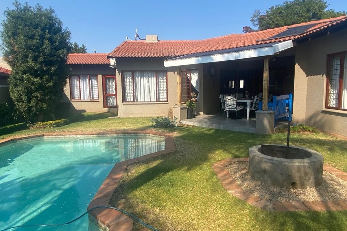 Rear view of the property featuring a swimming pool, a covered patio area, and a built-in fire pit set within a landscaped garden.