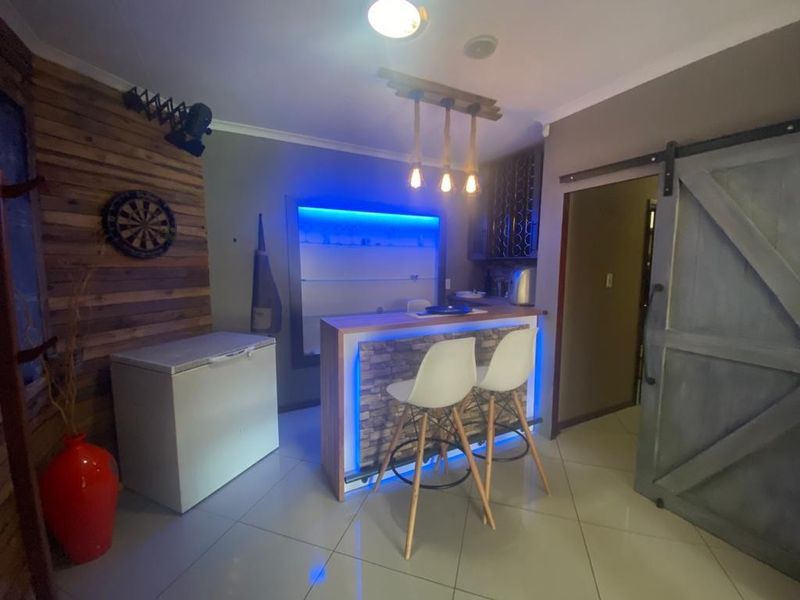 A modern home bar area featuring a built-in counter with LED accent lighting, tiled flooring, and a rustic sliding barn door.
