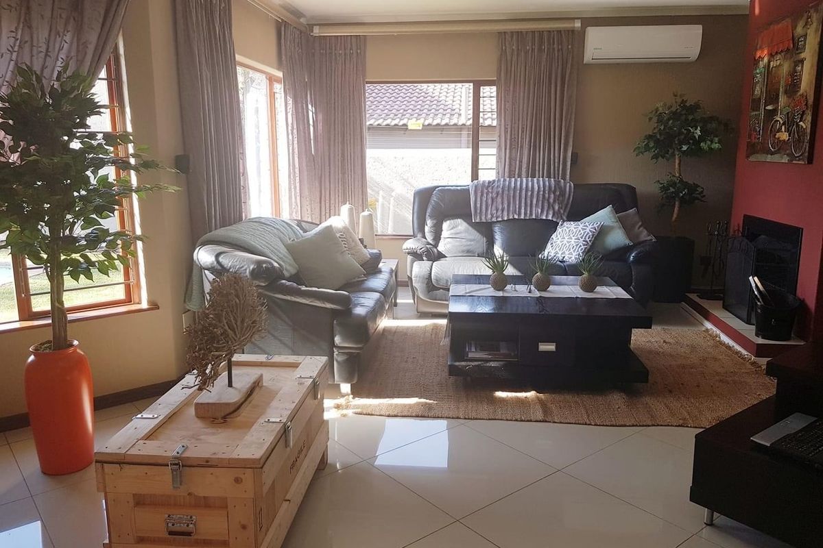 A comfortable living room featuring large windows, tiled flooring, a fireplace, and a wall-mounted air conditioning unit.