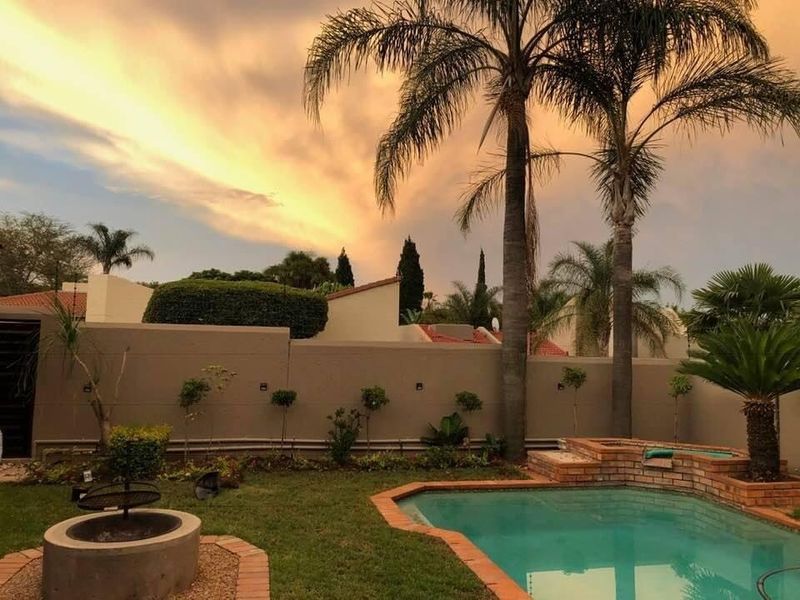 A well-maintained outdoor pool area featuring a swimming pool with brick coping, a built-in fire pit, and landscaped perimeter walls.