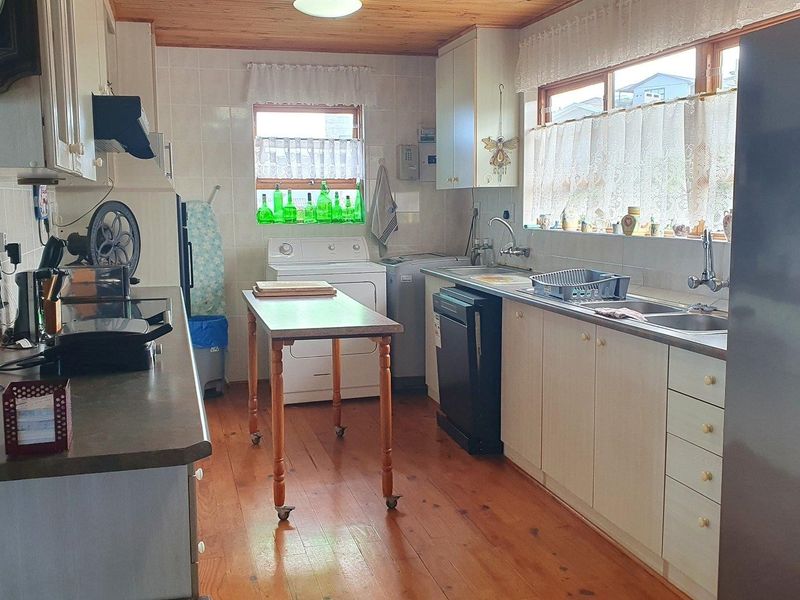 A functional kitchen featuring timber flooring, wood-paneled ceiling, tiled splashbacks, and ample built-in cabinetry with a double sink setup.