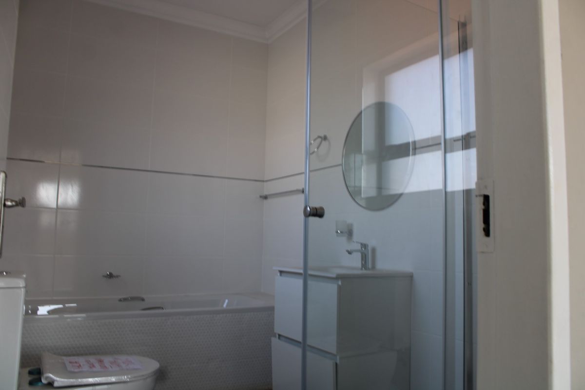 A clean, modern bathroom featuring a bathtub, a vanity unit, and a glass-enclosed shower with white wall tiling.